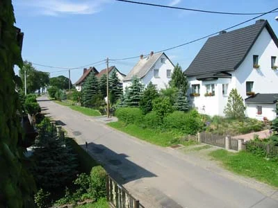 Häuser und Vorgärten entlang einer Straße an einem sonnigen Tag.