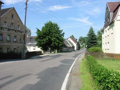 Eine Straße führt zwischen Häusern und Grünflächen hindurch.